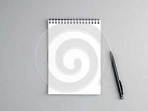 Blank sheet of notebook with a spiral and pen on a neutral gray