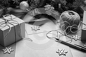 Blank sheet of paper, pen, gifts in handmade boxes, twine, artificial spruce branches and wooden snowflakes, black and