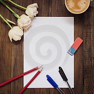 Blank sheet of paper, pencils, eraser, flowers and cup of coffee on dark wooden desk.