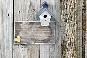 Blank sign with blue and white birdhouse next to tree