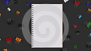 Blank spiral notebook with colorful binder clips on black table