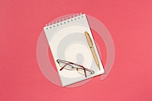 Blank spiral notebook, pen and glasses on the red background