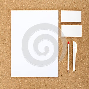 Blank Stationery on cork board. Consist of Business cards, A4 letterheads, pen and pencil.