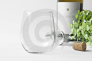 Blank stemless wine glass with wine bottle, bottle opener and greenery.