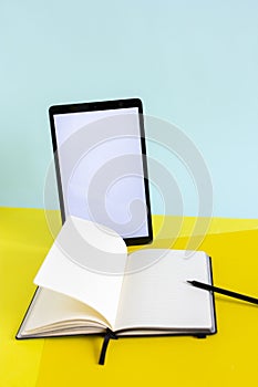 Blank tablet and ope notebook with pencil on yellow and blue background