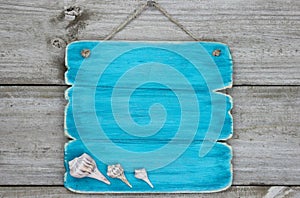 Blank teal blue sign with seashells hanging on rustic wooden door photo