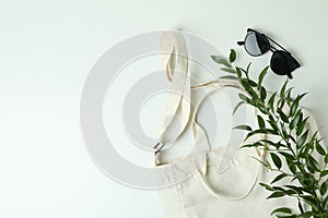 Blank textile bag, branch and sunglasses on white background
