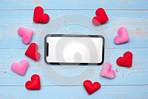 Blank touchscreen display of black smart phone with red and pink hearts shape decoration on blue wooden table background. Love,