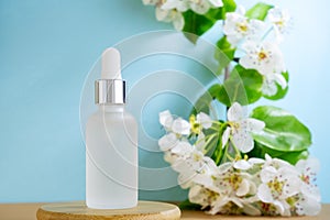 Blank transparent beauty serum dropper on blue background with blooming apple tree branch. Beauty care concept,selective focus