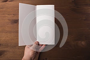 Blank tri fold brochure in hand on wooden background to replace your design or message