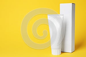 Blank tube of toothpaste and box on color background