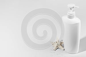 Blank unbranded bottle with dispenser and starfish on light shadow backdrop, copy space. Mockup style. White container for