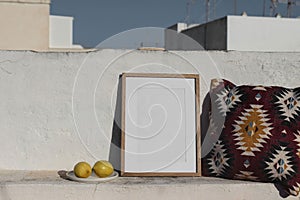 Blank vertical wooden frame picture mock up. Fresh lemon fruit, Mexican pattern cushion. White old textured white wall