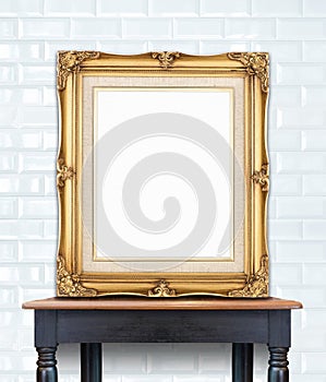 Blank vintage golden photo frame lean at ceramic tile wall on wood table