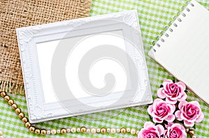 Blank vintage white photo frame and open diary with pink rose on
