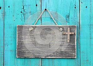 Blank weathered sign with wooden cross hanging by rope on antique teal blue wood door