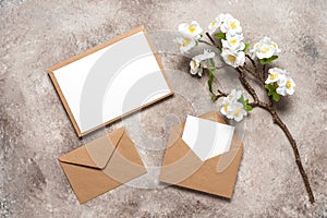 Blank wedding card mockup in brown envelopes and cherry blossom branch artificial. Beige grunge background. Spring stationery