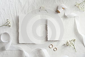 Blank wedding invitations cards mockups with space for text, golden rings, ribbon flowers on white textile background. Flat lay,