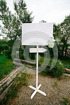 Blank wedding white banner with arrow sign decorated by flowers on stand outdoor. Copy space for your text.