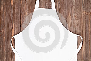 Blank white apron template on wooden background, copy space. Kitchen, cooking clothing mockup photo