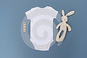 Blank white baby bodysuit grow mockup with cream rabbit soft toy and `baby` written in wooden tiles on a light blue background photo