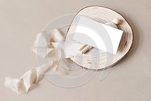 Blank white business card mockup on wooden plate with spool and silk ribbon. Beige table backgound. Branding identity