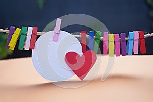 Blank white circle paper with red heart and colorful wooden paper clips on rope.