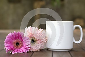 Blank white coffee cup and flowers. A cup of morning coffee or tea with soft pink and purple daisy flowers on the table.