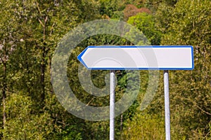 Blank white directional arrow sign on nature background. Blank road sign on the road
