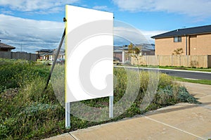 Blank white empty mockup template of a real estate sign at front of a lot of vacant land in a suburban neighbourhood