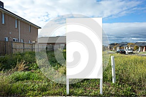 Blank white empty mockup template of a real estate sign at front of a lot of vacant land on a suburban neighbourhood street