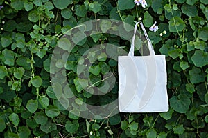 Blank white fabric cloth bag tote at green bush trees foliage