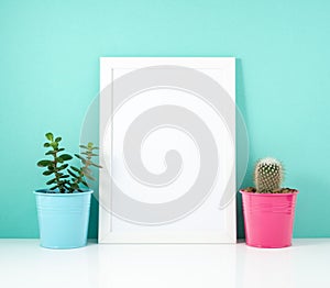 Blank white frame, plant cactus on white table against the blue wall. Mockup with copy space.