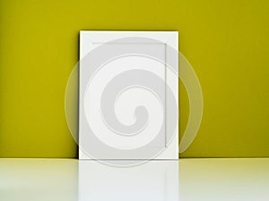 Blank white frame on a white table against the olive colored wall