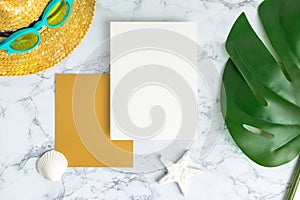 Blank white and gold paper card on marble table top view with summer beach accessories and shell,starfish,tropical palm leaves