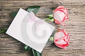 Blank white greeting paper card with pink roses and ribbon on old wooden table - Love Concept