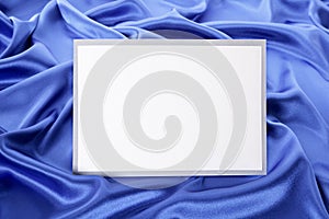 Blank white greetings card or invitation with blue satin background, copy space