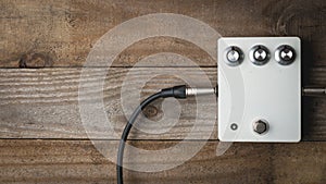 A blank white guitar pedal with vintage knobs and plugged jacks on wooden floor