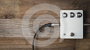 A blank white guitar pedal with vintage knobs and plugged jacks on wooden floor photo