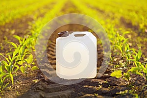 Blank white herbicide canister can in corn seedling field in springtime sunset