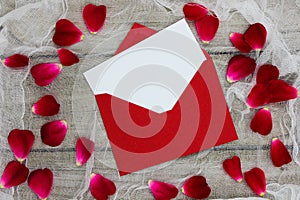 Blank white love letter and red envelope surrounded by red rose petals