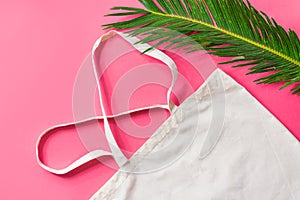 Blank white mockup linen cotton cloth tote bag green palm leaf on fuchsia pink background trendy flat lay. Zero waste reusable eco
