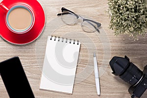 Blank white notebook open, eyeglass, pen and cup of coffee on the desk