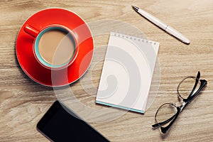 Blank white notebook open, eyeglass, pen and cup of coffee on the desk