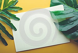 Blank white notepaper with tropical leaves laying on yellow table