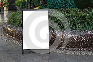 Blank white outdoor advertising stand mock up template. Clear street signage board placed against green plants.