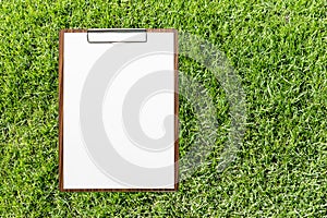 Blank white papaer on wooden clipboard with space on green grass background