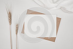 Blank white paper on brown paper envelope with Barley dry flower and white cloth. Mock-up of horizontal blank greeting card. Top