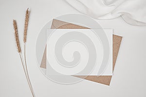 Blank white paper on brown paper envelope with Bristly foxtail dry flower and white cloth. Mock-up of horizontal blank greeting