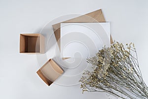 Blank white paper on brown paper envelope with Limonium dry flower and Carton box. Mock-up of horizontal blank greeting card. Top